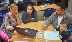 Father with two daughters and their mentor, looking at a computer in a classroom setting